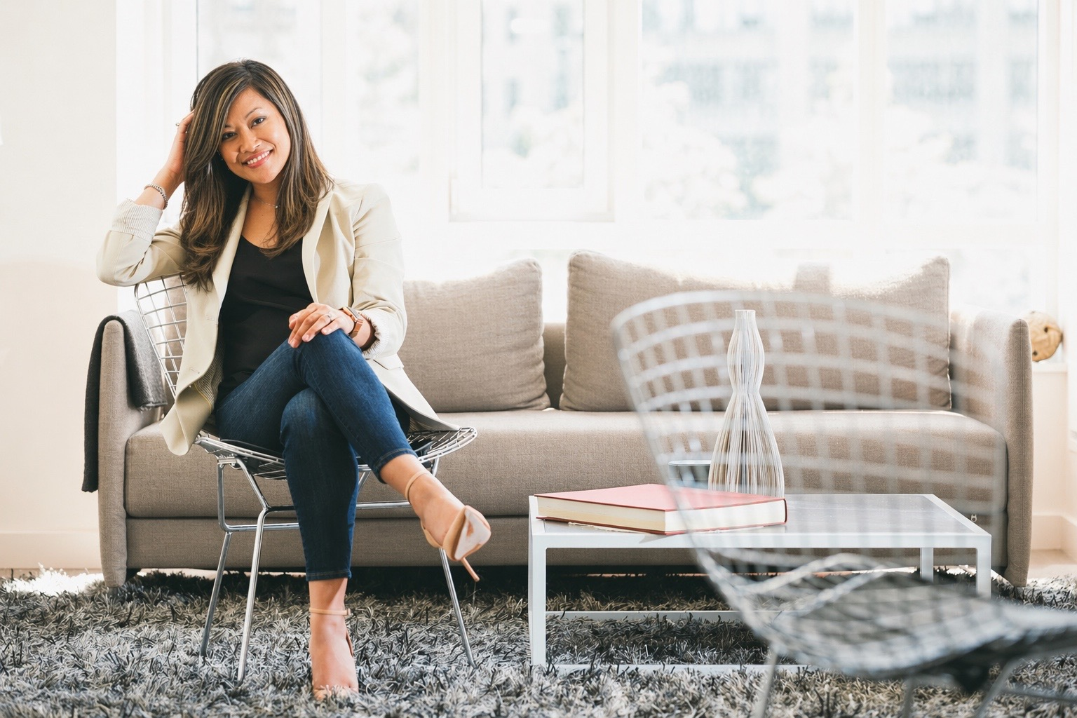 Sara Llanes seated on a neutral-toned couch in a bright studio setting.